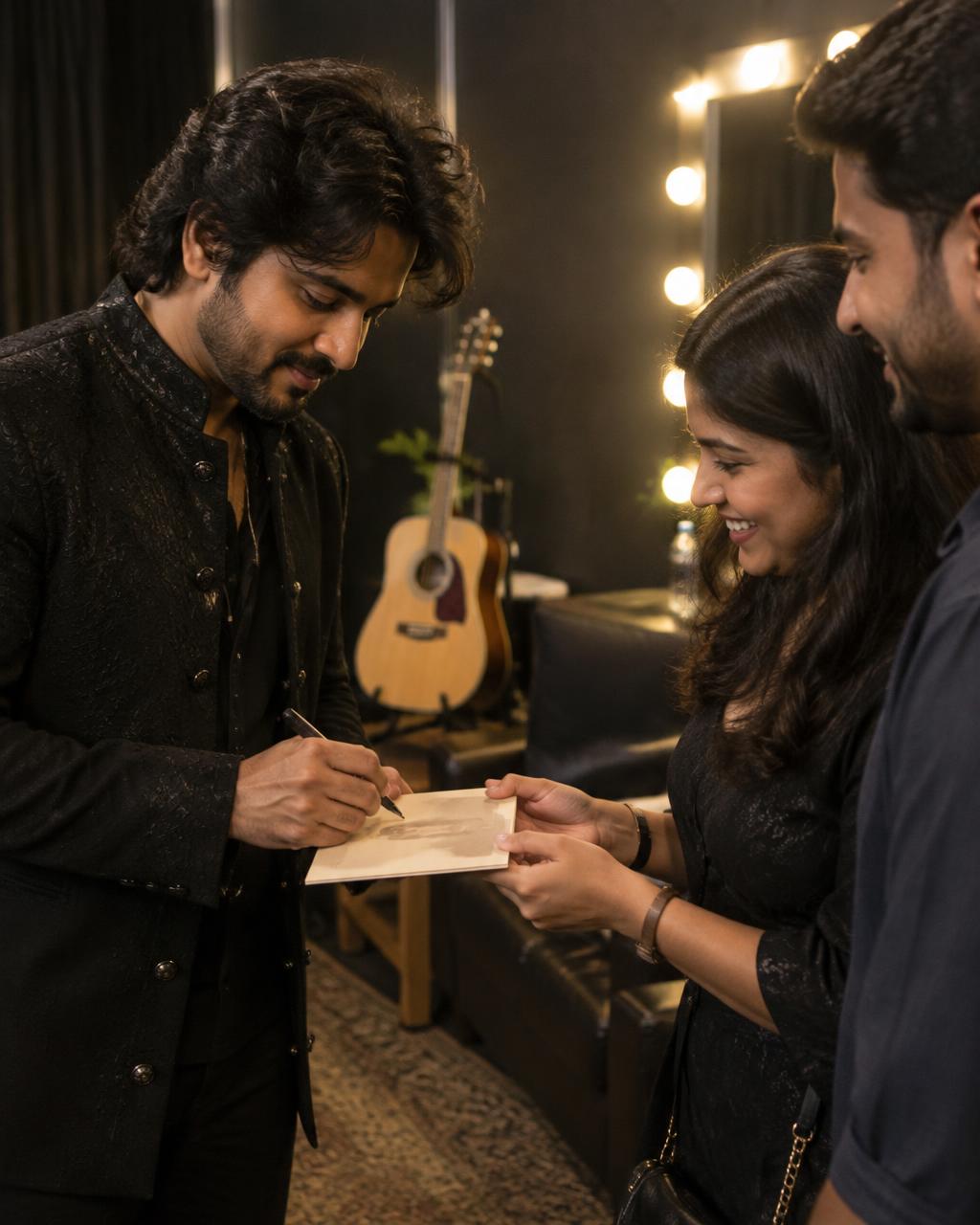 A musician signs a keepsake for guests beside an acoustic guitar backstage.